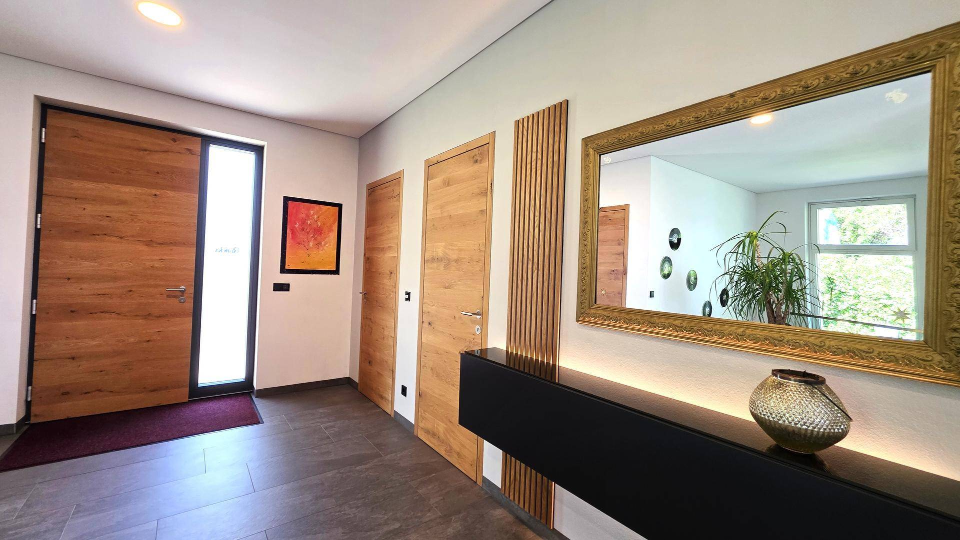Heller Eingangsbereich mit Holztüren, großem Spiegel und moderner Konsole, die zum Wohnbereich führt.
