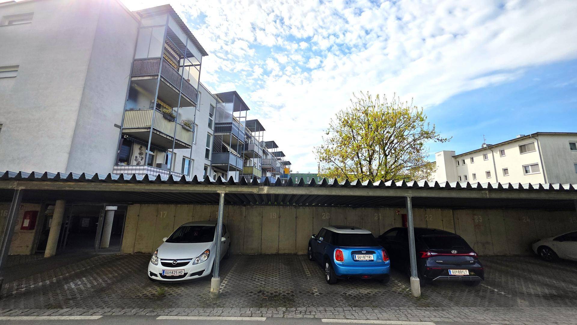 Überdachter Parkplatzbereich mit mehreren Stellplätzen vor einem Wohngebäude mit Balkonen.