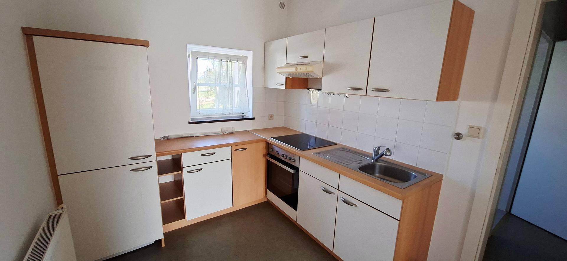 Kleine Einbauküche mit weißen Schränken, Kochfeld und Kühlschrank.