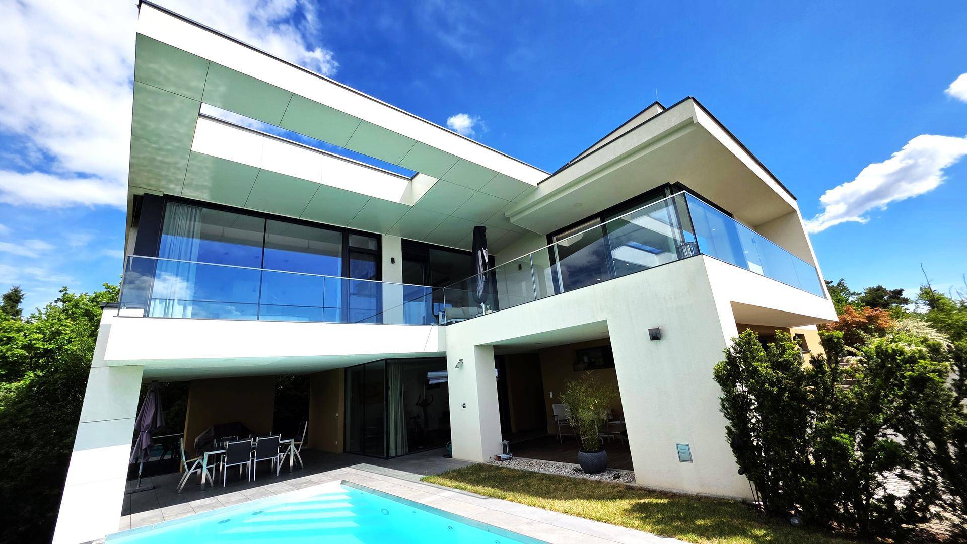 Elegante moderne Villa mit großen Glasfronten und klaren Linien unter blauem Himmel.
