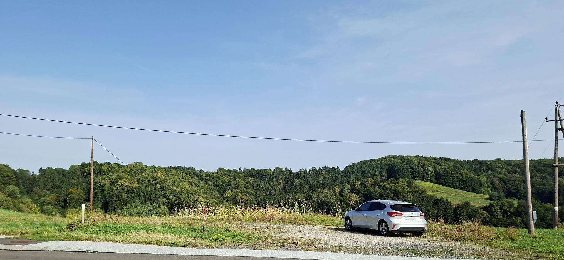 Ein Auto parkt auf einem Schotterplatz neben einer Straße mit Panoramablick auf grüne Hügel und Wälder.