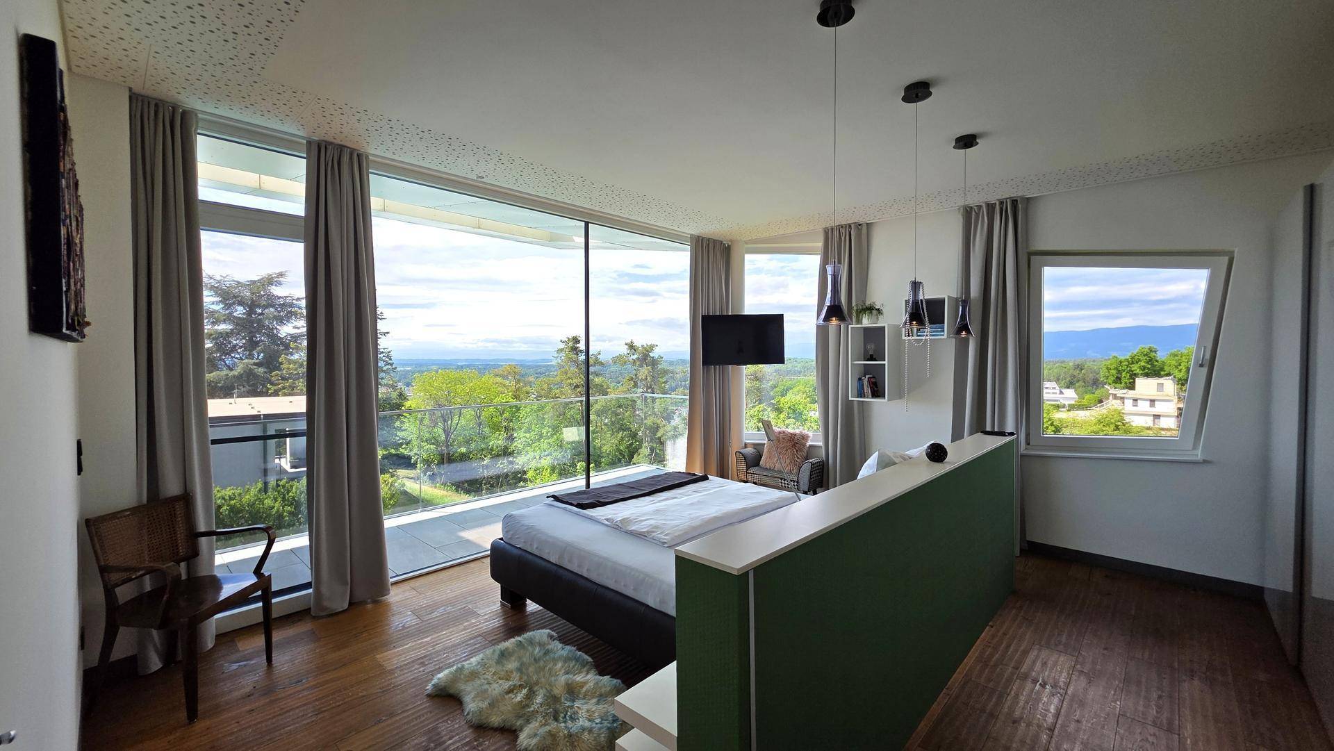 Helles Schlafzimmer mit Holzboden, bodentiefen Fenstern und Panoramablick auf die umliegende Landschaft.