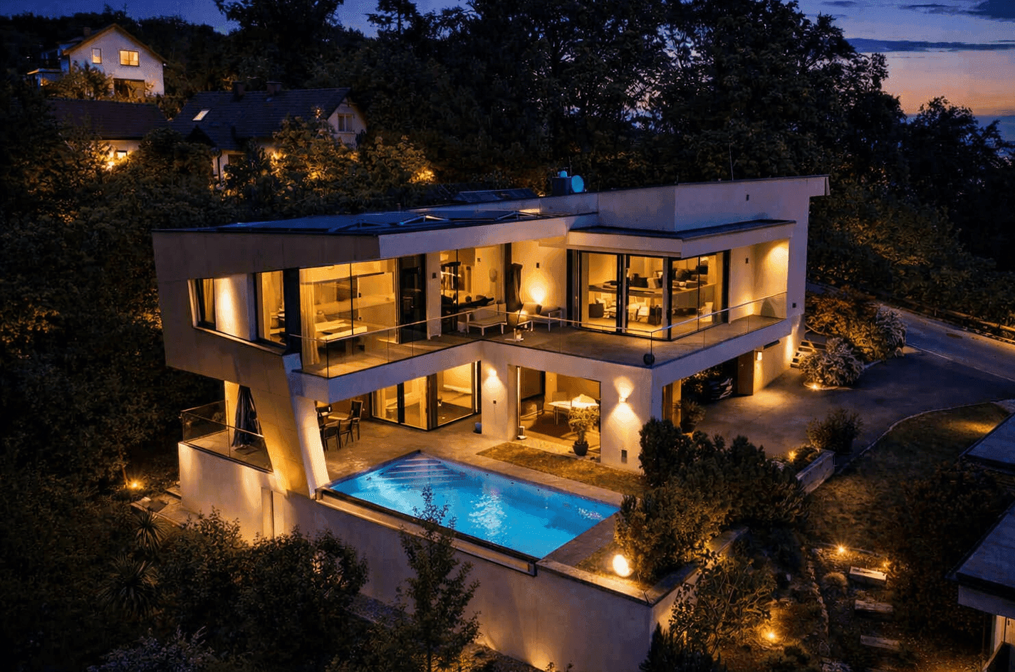 Moderne Villa bei Nacht mit beleuchteten Terrassen, großzügigen Glasfronten und einem Infinity-Pool.
