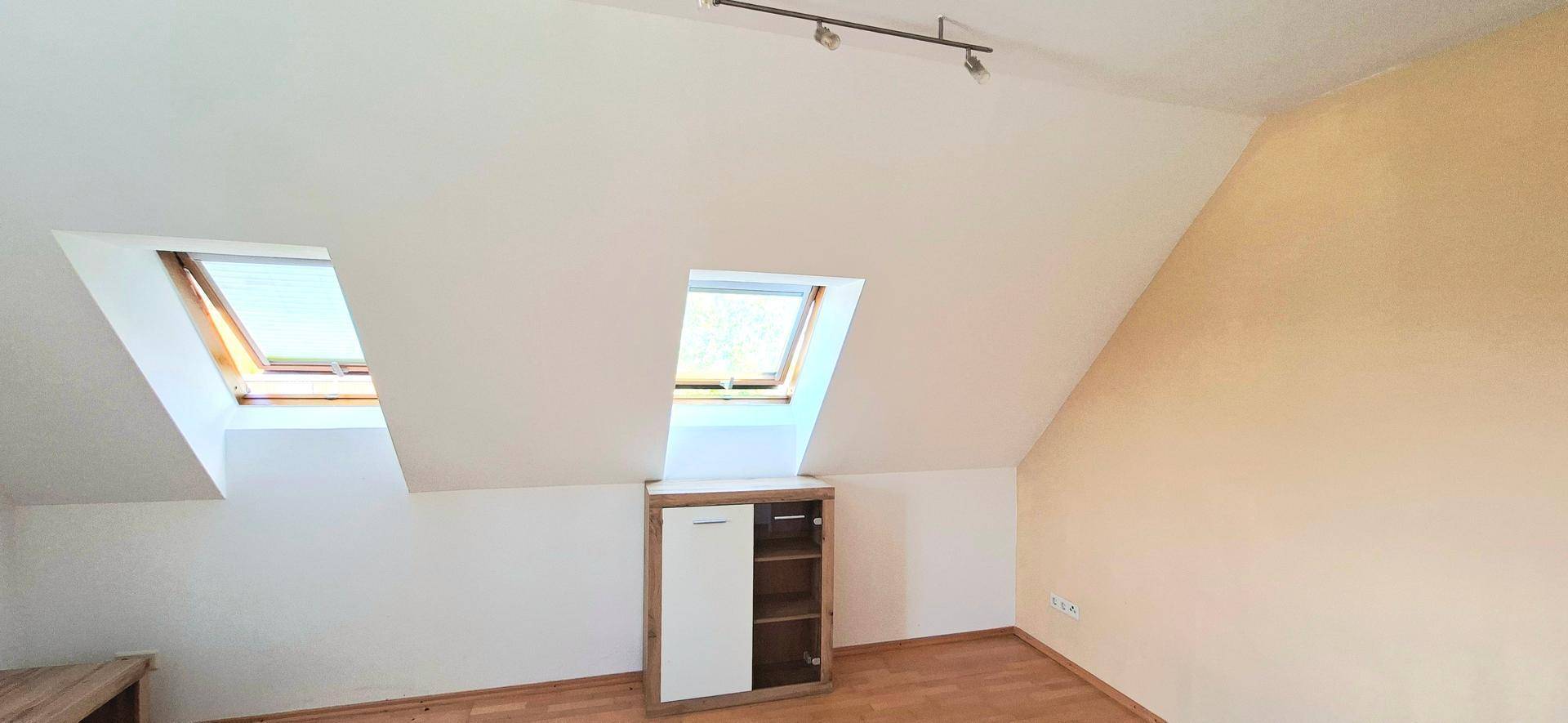 Dachgeschosszimmer mit Holzboden, Dachschrägen und zwei hellen Dachfenstern.