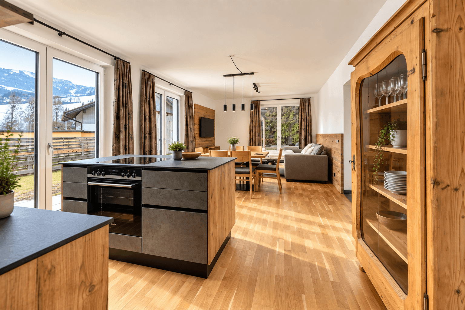 Offener Wohn-Essbereich mit moderner Küche, Holzboden und großen Fenstern mit Bergblick.