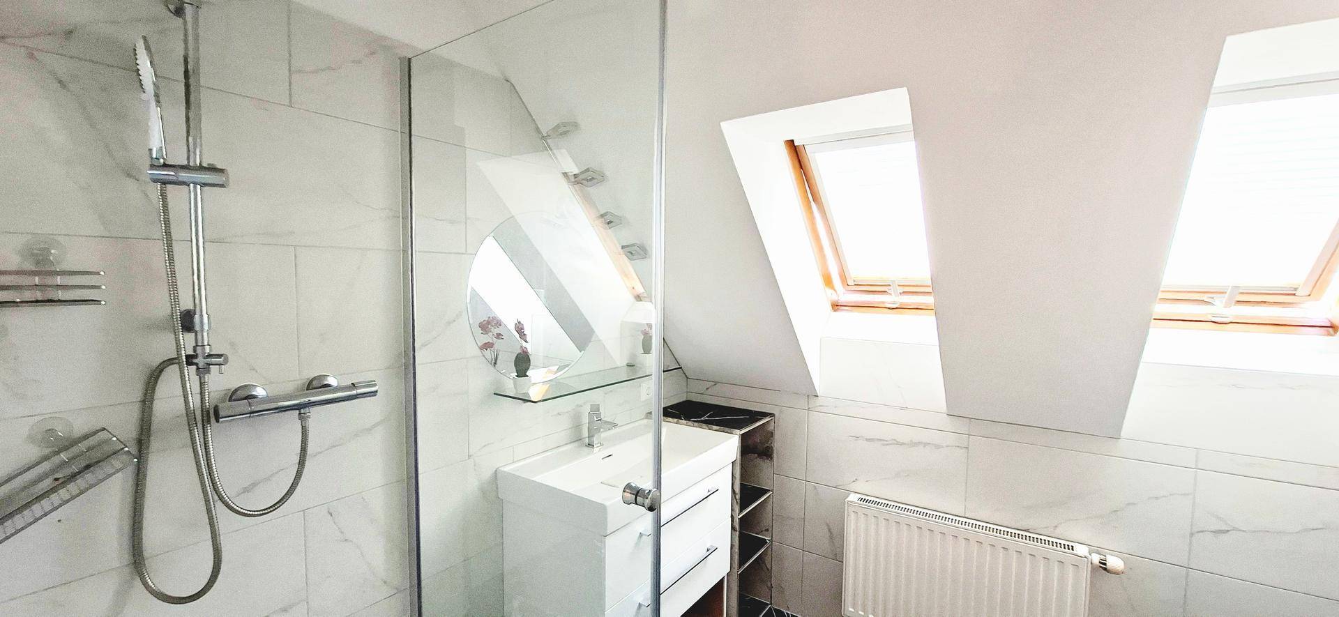 Modernes Badezimmer im Dachgeschoss mit Duschkabine, Waschbecken und Dachfenstern.