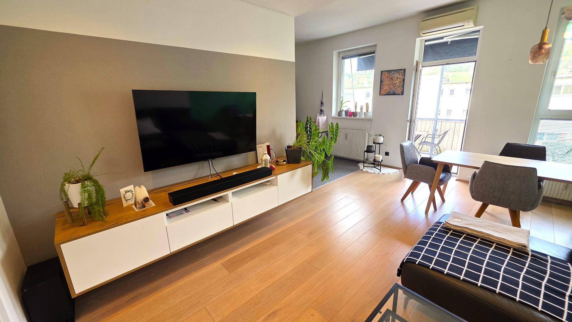 Geräumiger Wohnbereich mit großem Fernseher, Holzboden und Zugang zu einem Außenbereich.