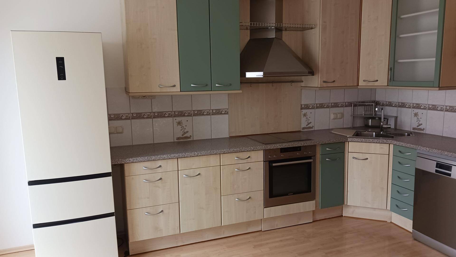 Funktionale Einbauküche mit Holzfronten, grünen Oberschränken und integrierten Küchengeräten.