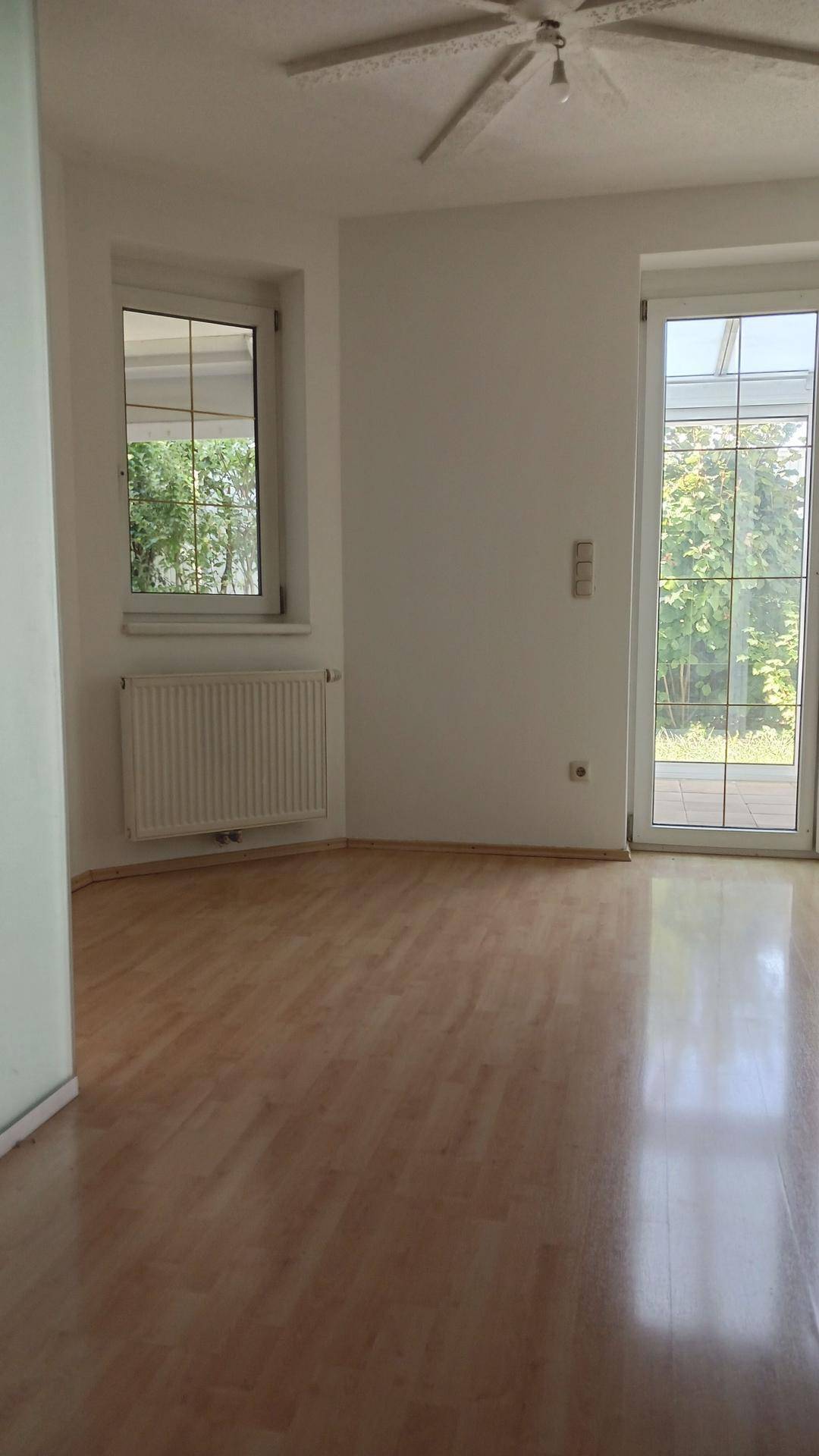Geräumiges Wohnzimmer mit Laminatboden, Fenster und großer Glasschiebetür zum Garten.