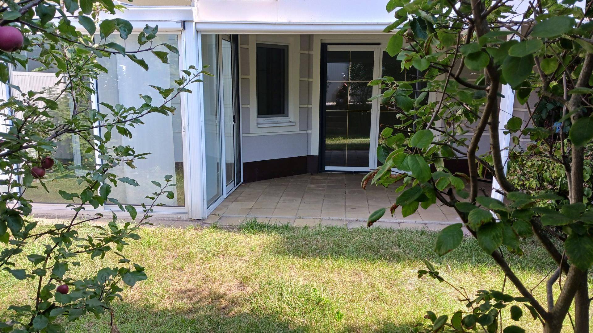 Gedeckte Terrasse mit Fliesenboden und Zugang zum Garten, umgeben von grünen Pflanzen.
