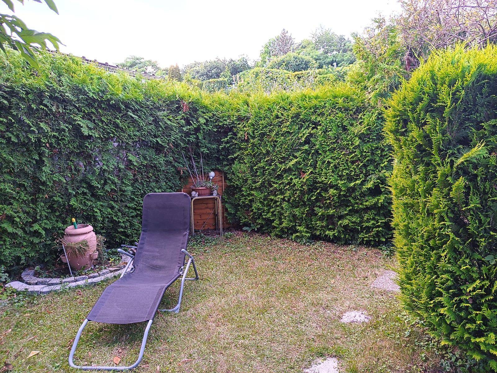 Kleiner, privater Gartenbereich mit Liegestuhl, umgeben von hohen Hecken.