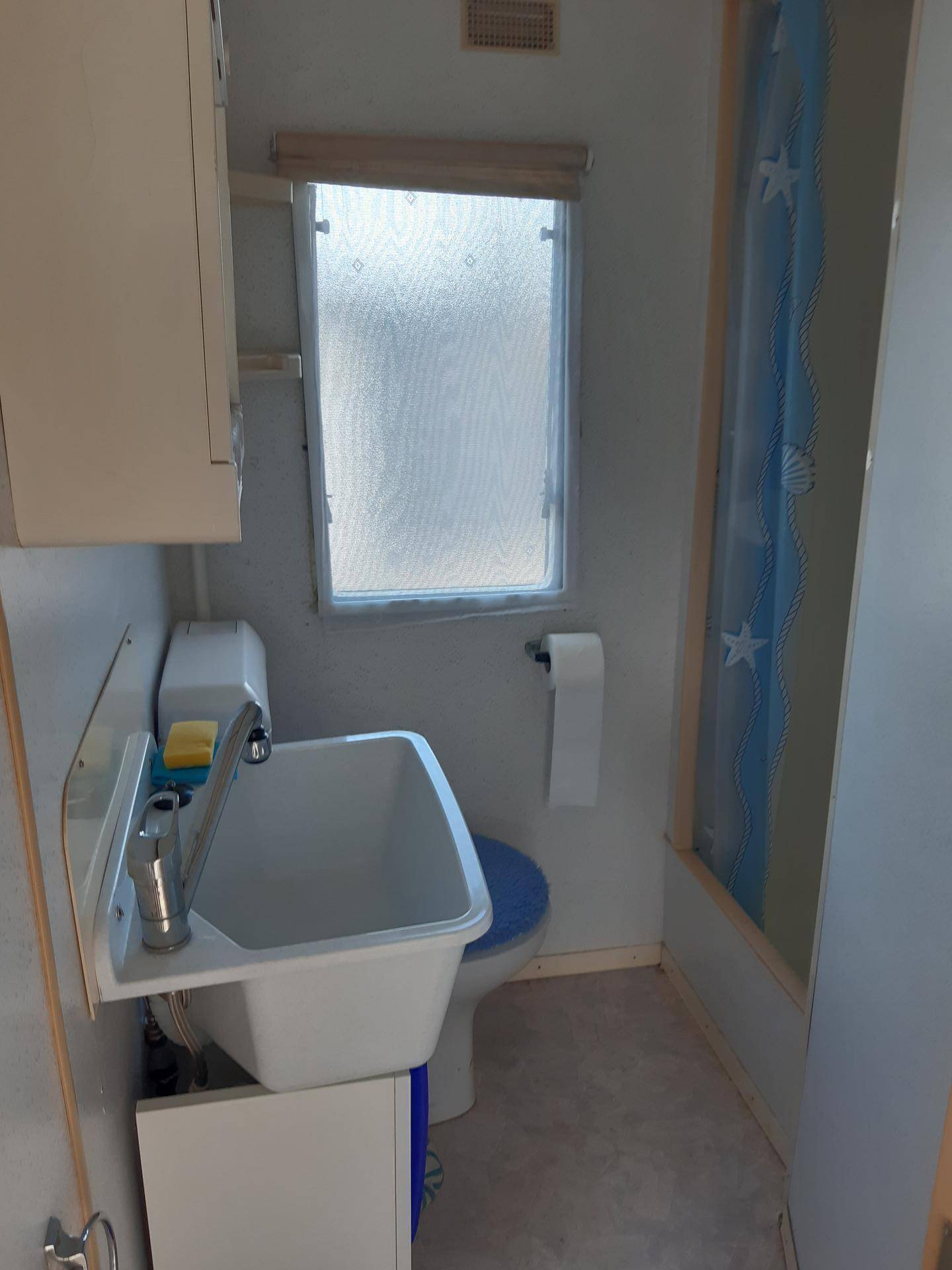 Kleines Badezimmer mit Waschbecken, Toilette und Duschbereich mit Vorhang.