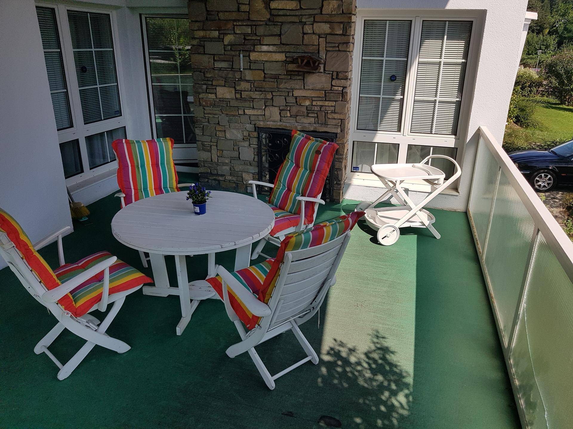 Gemütlicher Balkon mit bunten Sitzkissen, weißem Tisch und Steinwand.