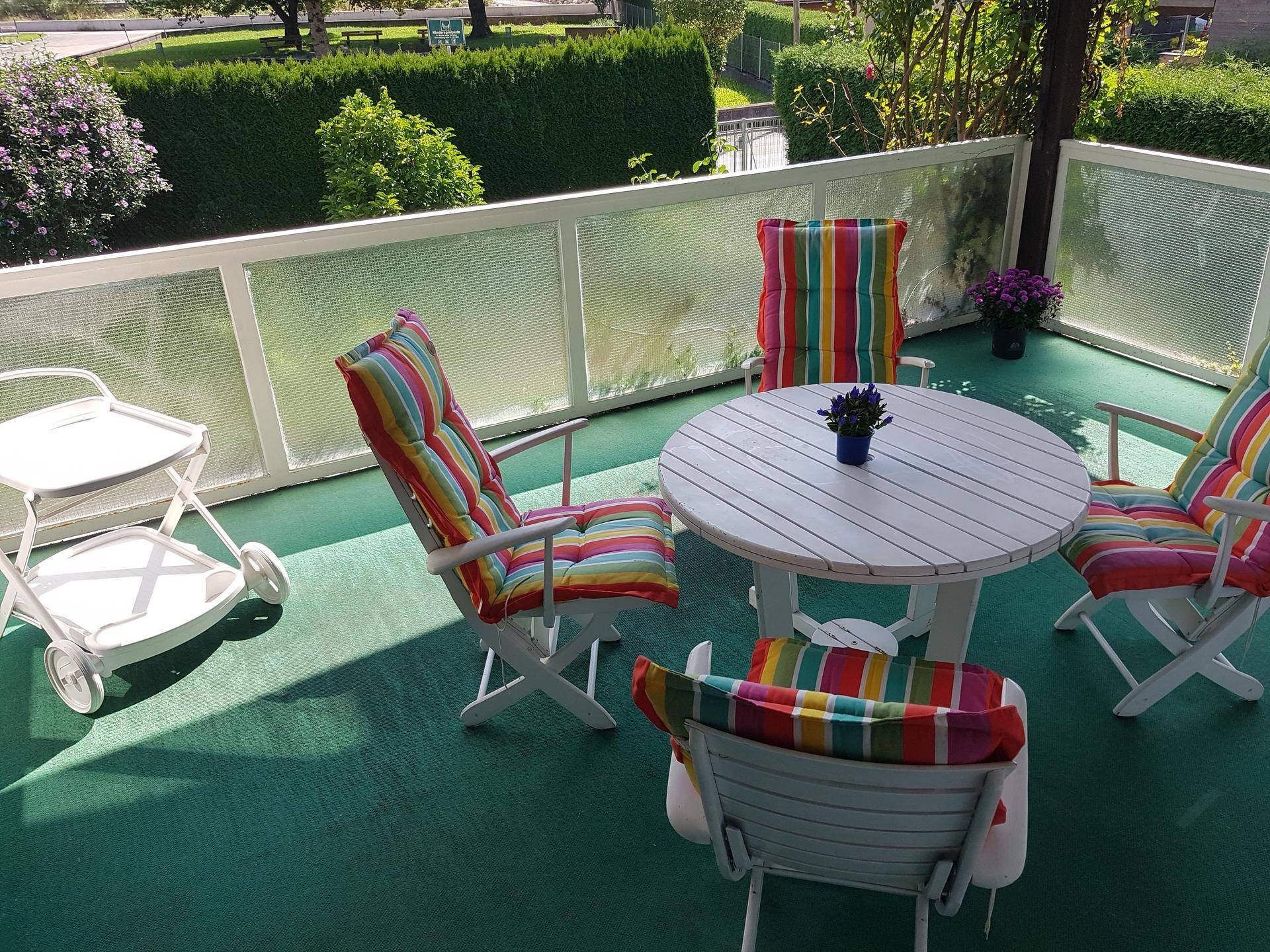 Heller Balkon mit Gartenmöbeln und Blick ins Grüne, umgeben von einer Hecke.