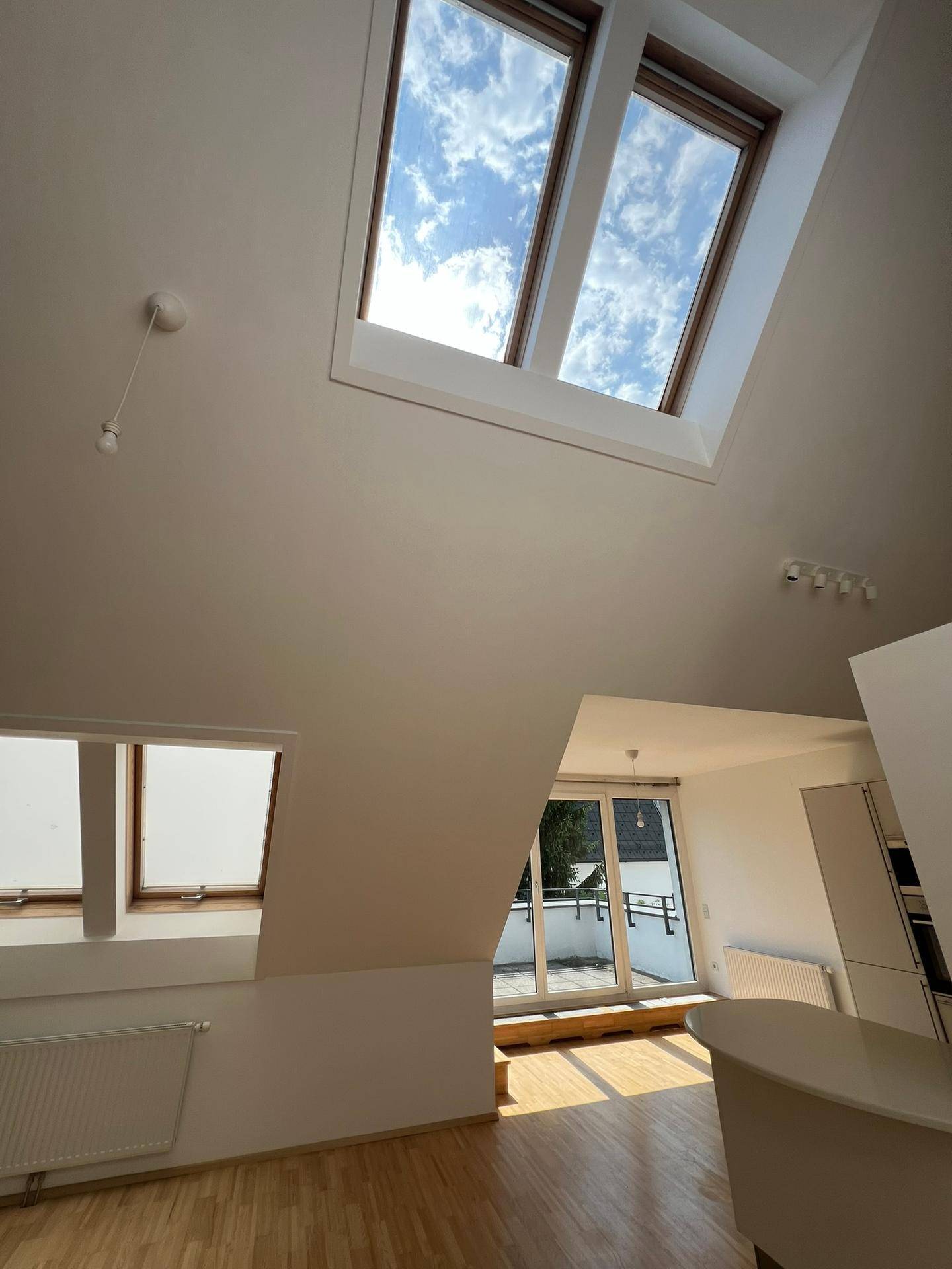 Heller Raum mit hohen Decken, Dachfenstern und Blick auf den Wohnbereich und die Terrasse.