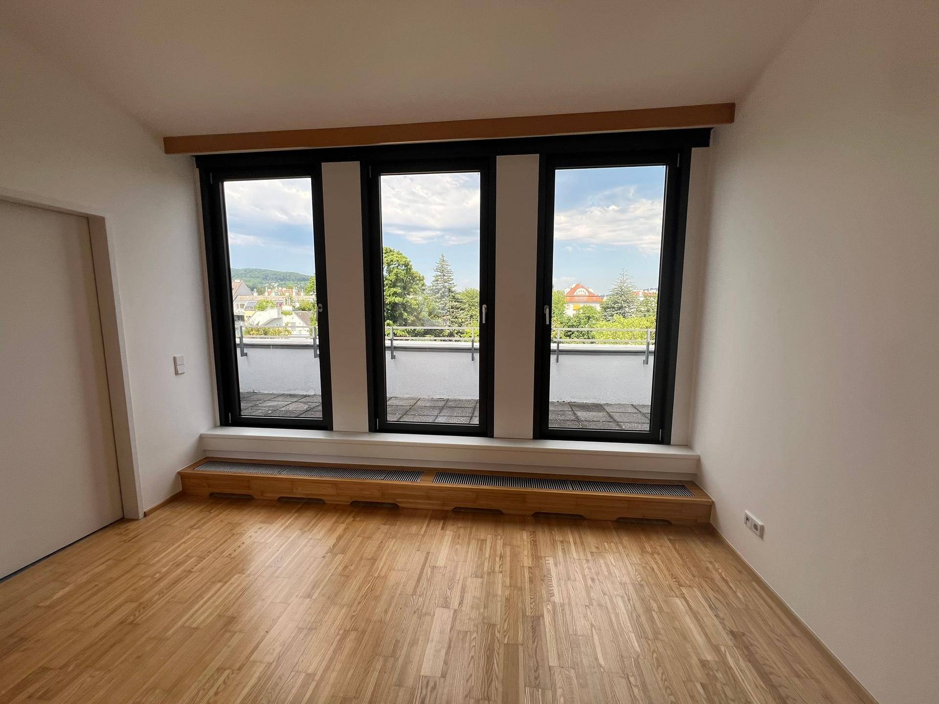 Geräumiges Zimmer mit großen Fenstern, Holzboden und direktem Zugang zu einer Terrasse.