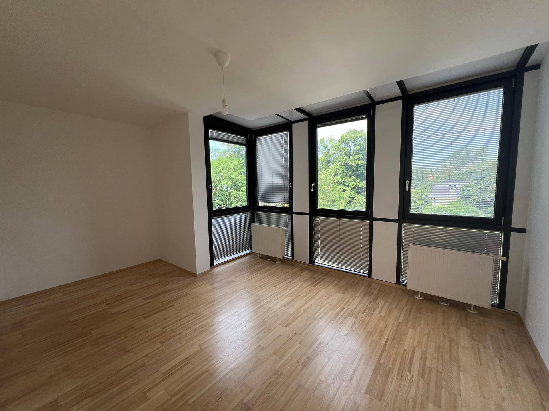 Geräumiges Zimmer mit vielen Fenstern, Holzboden und einem schönen Blick ins Grüne.