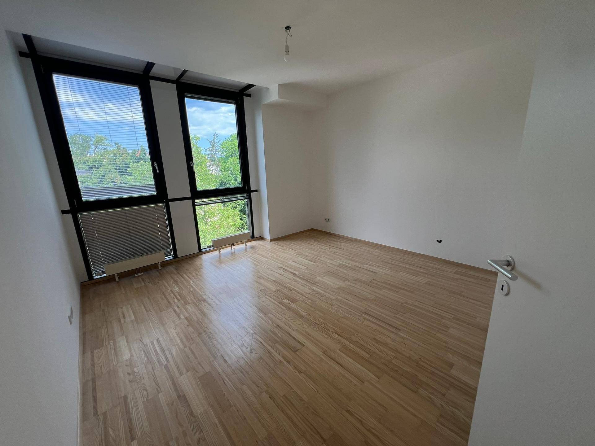 Helles Schlafzimmer mit Holzboden und Fenstern, die einen angenehmen Blick ins Grüne bieten.