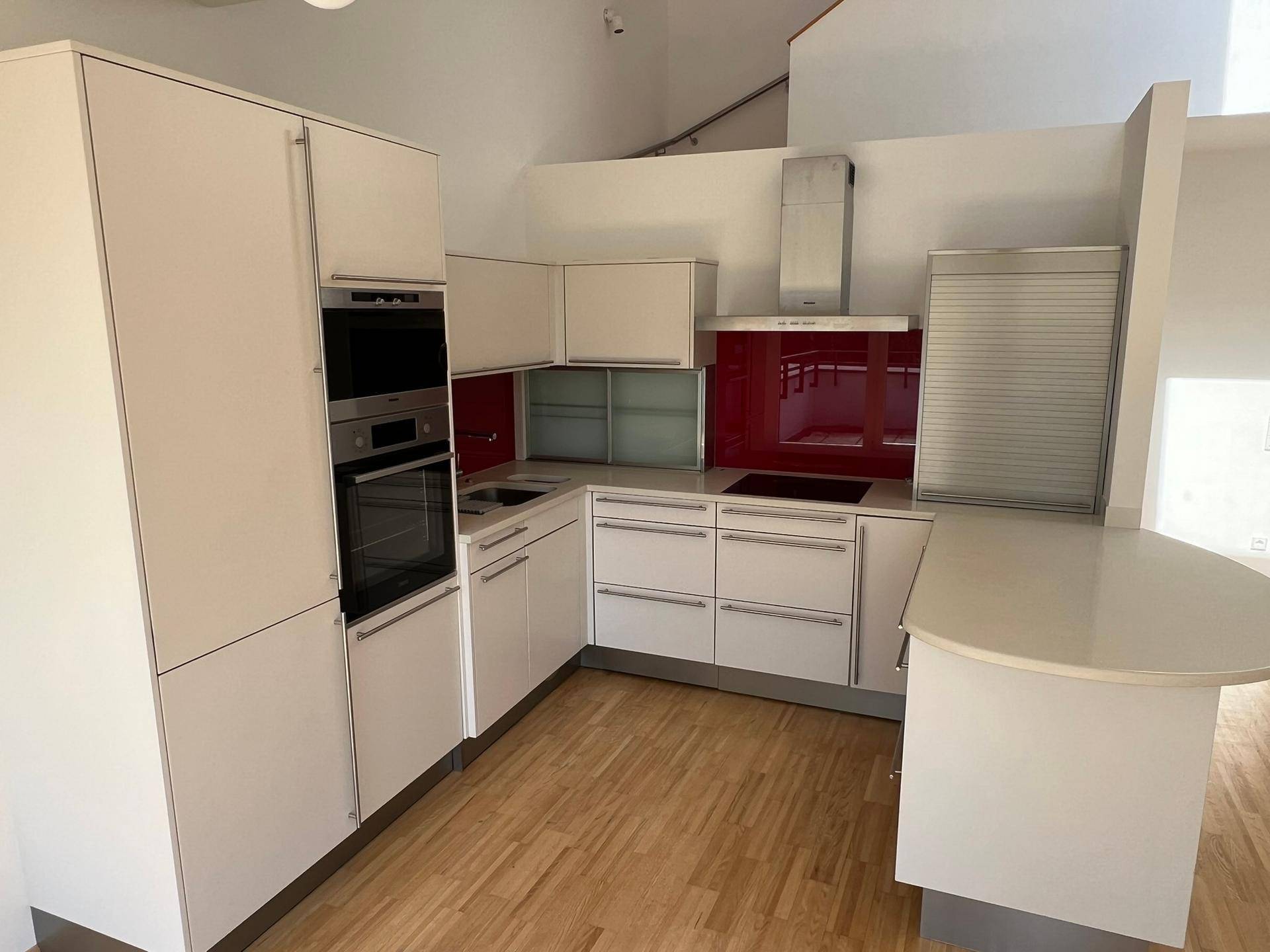 Moderne Einbauküche mit weißen Hochglanzfronten, roten Akzenten und Holzboden in offener Gestaltung.