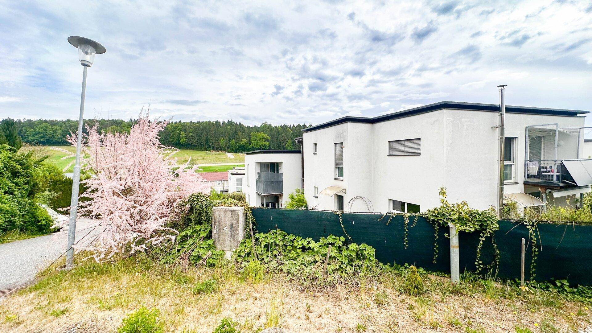 Panoramablick auf moderne Wohngebäude und die umliegende grüne Landschaft mit blühenden Bäumen.
