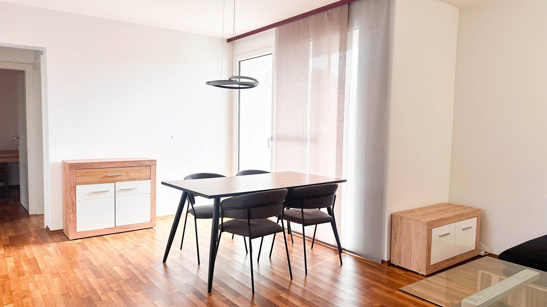 Heller Essbereich mit Holztisch und modernen Stühlen, angrenzend an den Wohnbereich.
