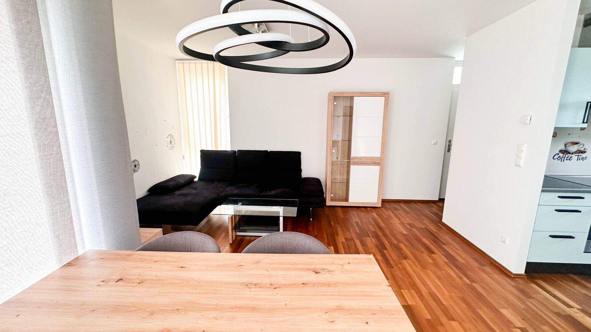 Offener Wohn- und Essbereich mit Holzboden, modernem Sofa und Esstisch.