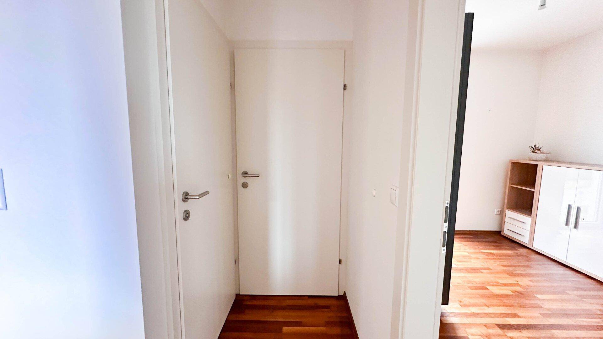 Heller Flur mit weißer Tür und Holzboden, der zu den weiteren Räumen führt.