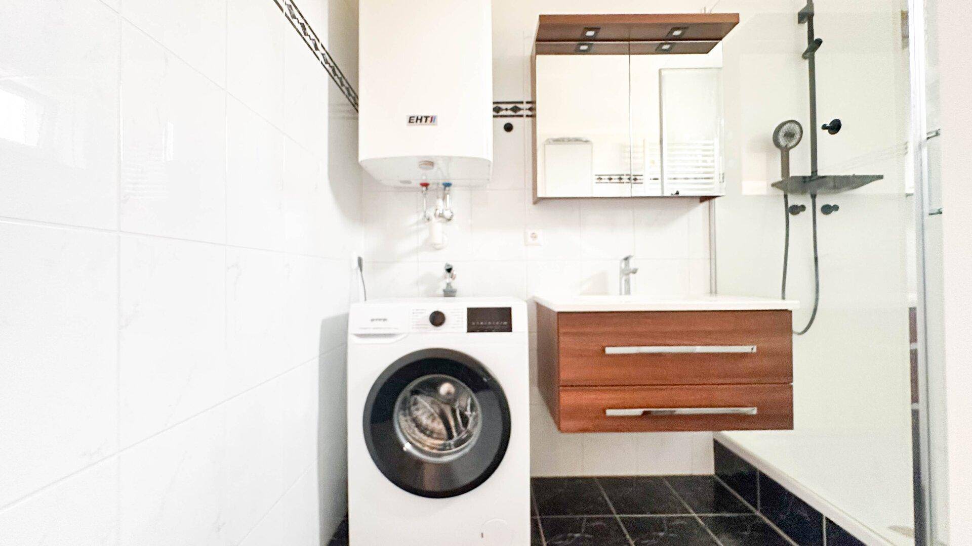 Modernes Badezimmer mit Waschmaschine, Waschbecken und Duschbereich, gefliest in Weiß und Schwarz.