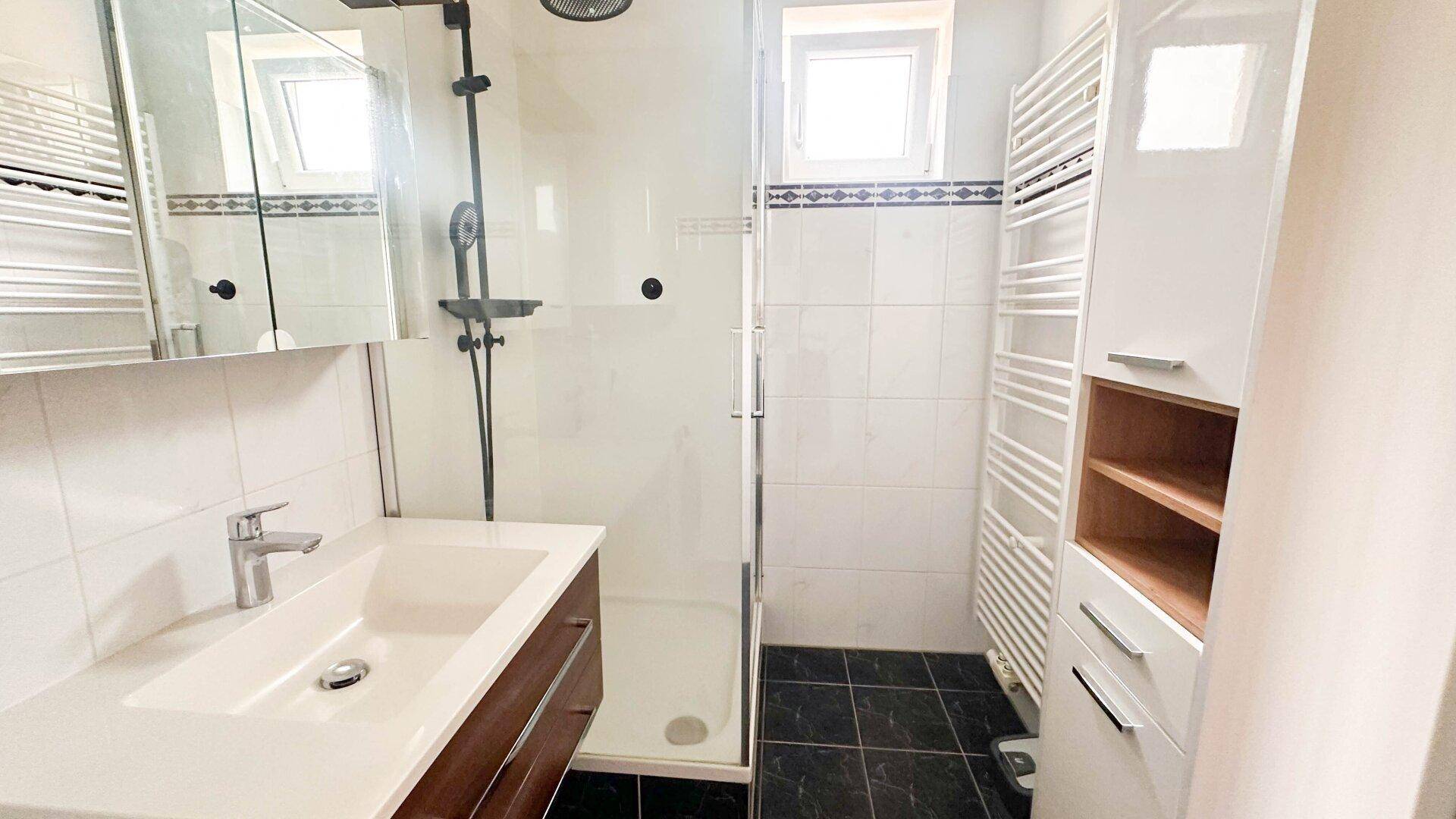 Helles Badezimmer mit Duschkabine, Waschbecken und beheiztem Handtuchhalter, gefliest in Weiß und Schwarz.
