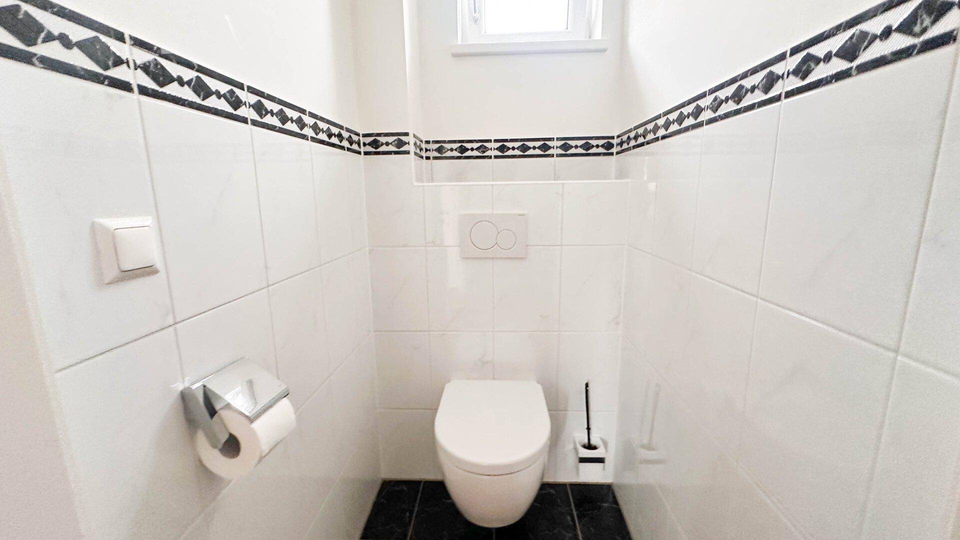 Separates WC mit wandhängender Toilette und Fliesen in Weiß und Schwarz.