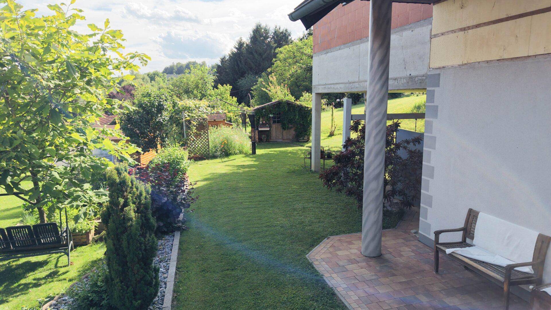 Gepflegter Garten mit Rasenfläche und überdachtem Sitzbereich neben dem Haus.