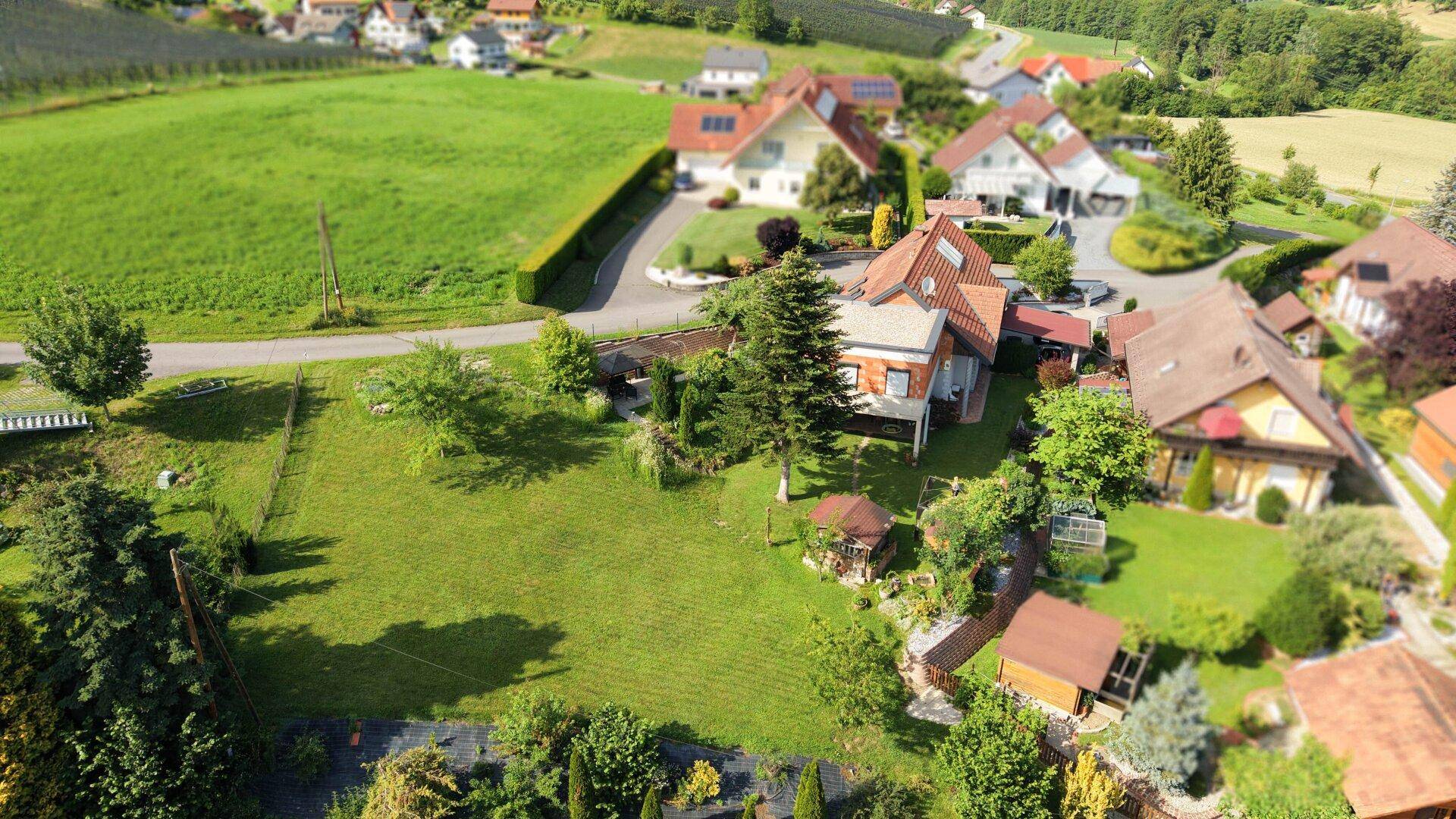 Weitläufige Luftaufnahme einer Wohnsiedlung mit viel Grün und Feldern im Hintergrund.