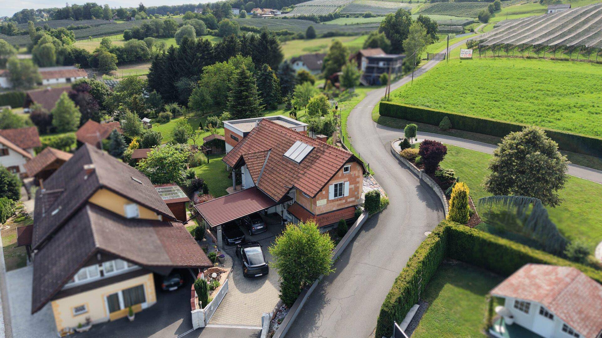 Luftaufnahme eines Wohnhauses mit Carport und gepflasterter Auffahrt in grüner Umgebung.