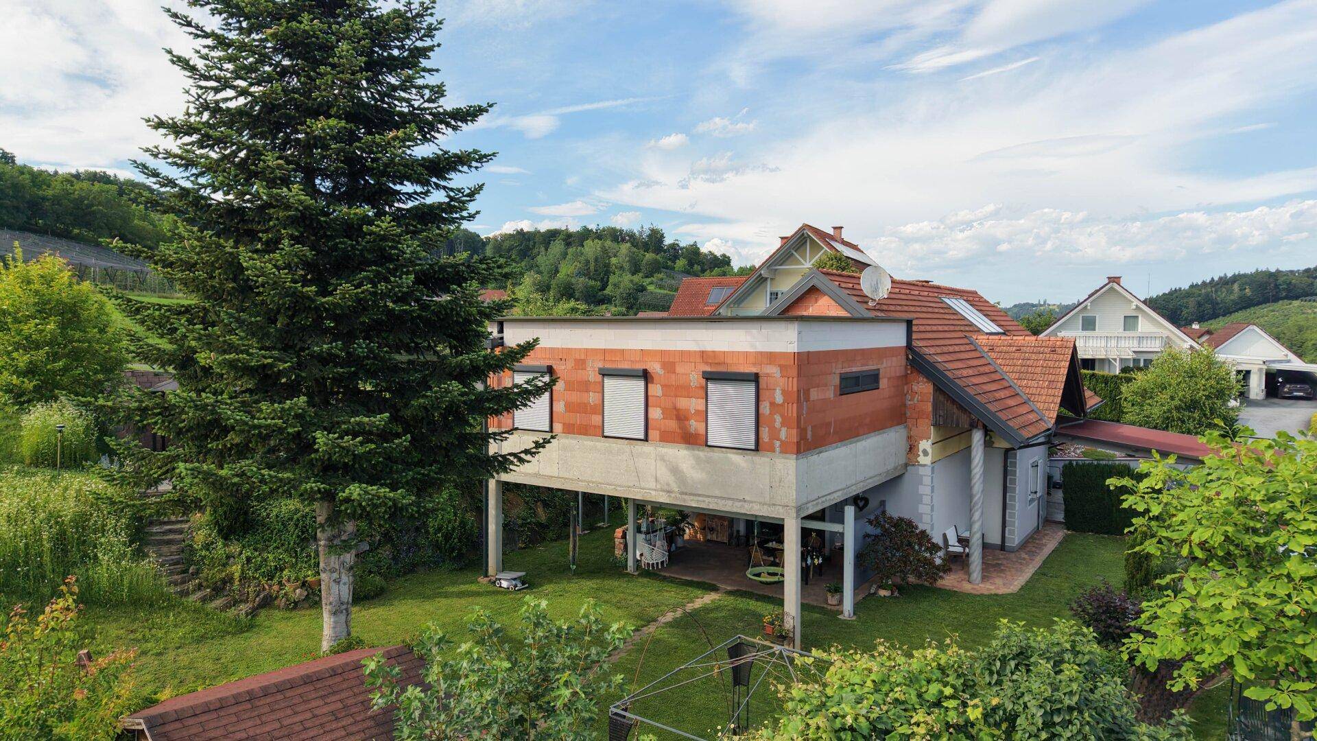 Ansicht des Hauses mit moderner Erweiterung, Flachdach und großem Baum im Vorgarten.