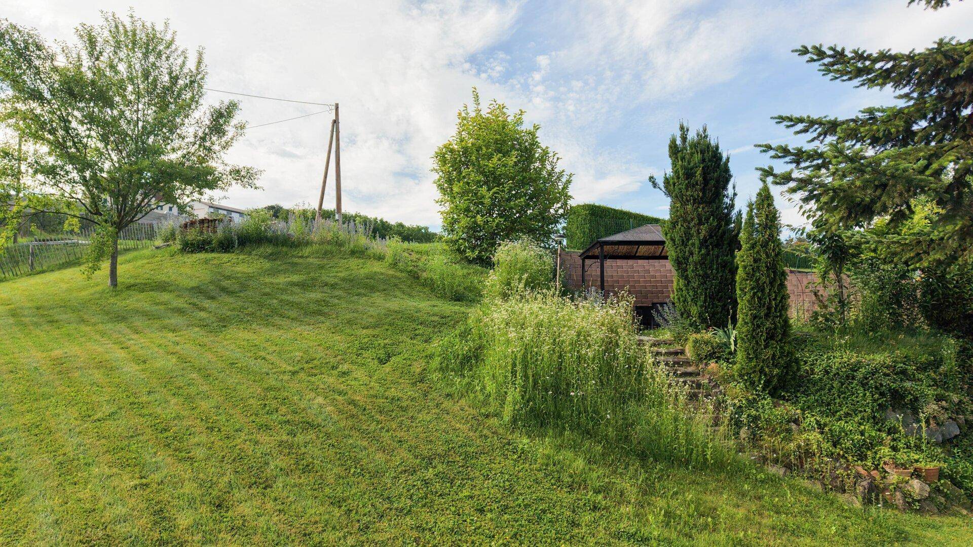 Großer, hügeliger Gartenbereich mit Rasen und einem Gartenpavillon im Hintergrund.
