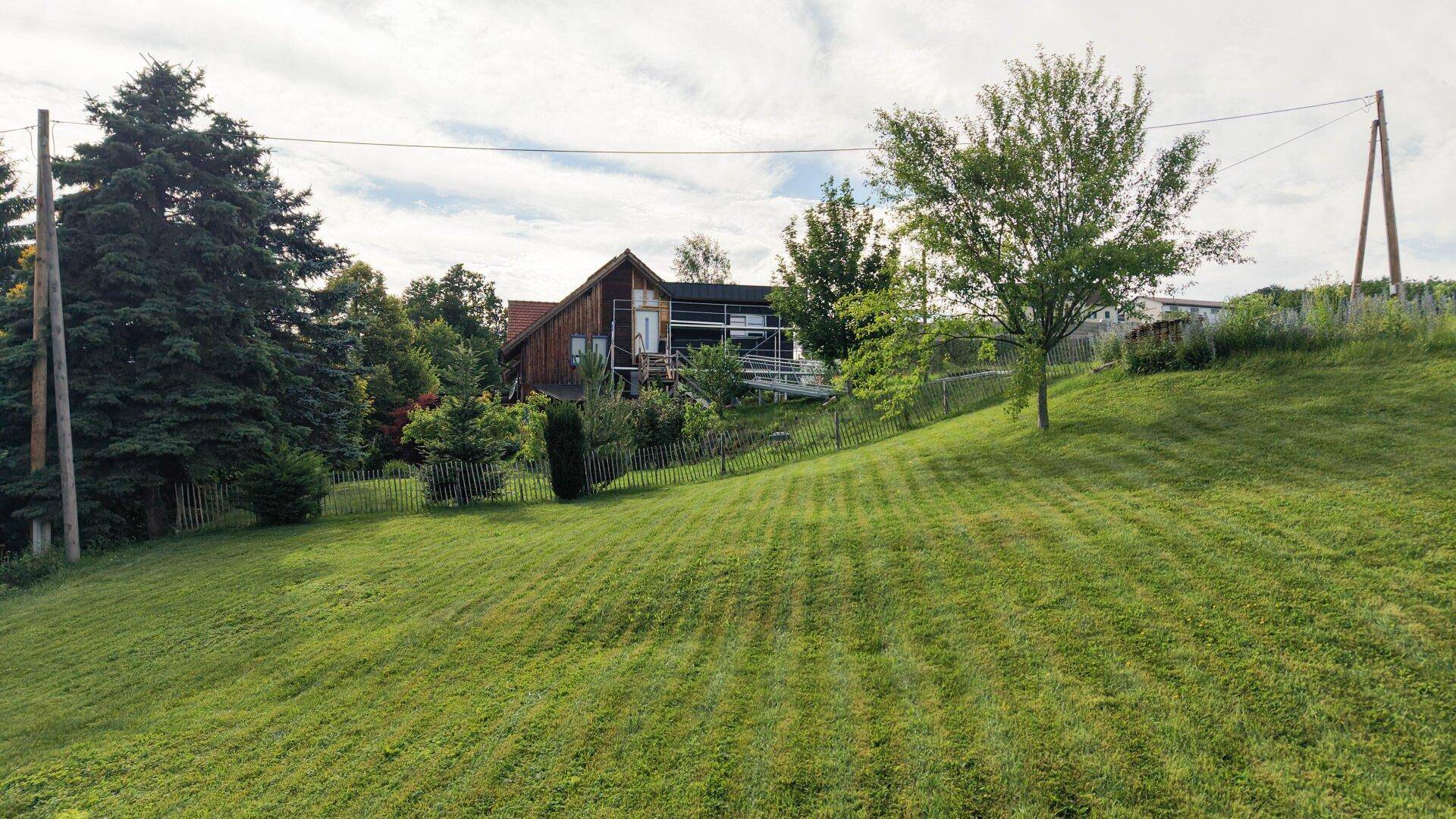 Weitläufige Rasenfläche eines Gartens mit Blick auf ein weiteres Gebäude in der Ferne.