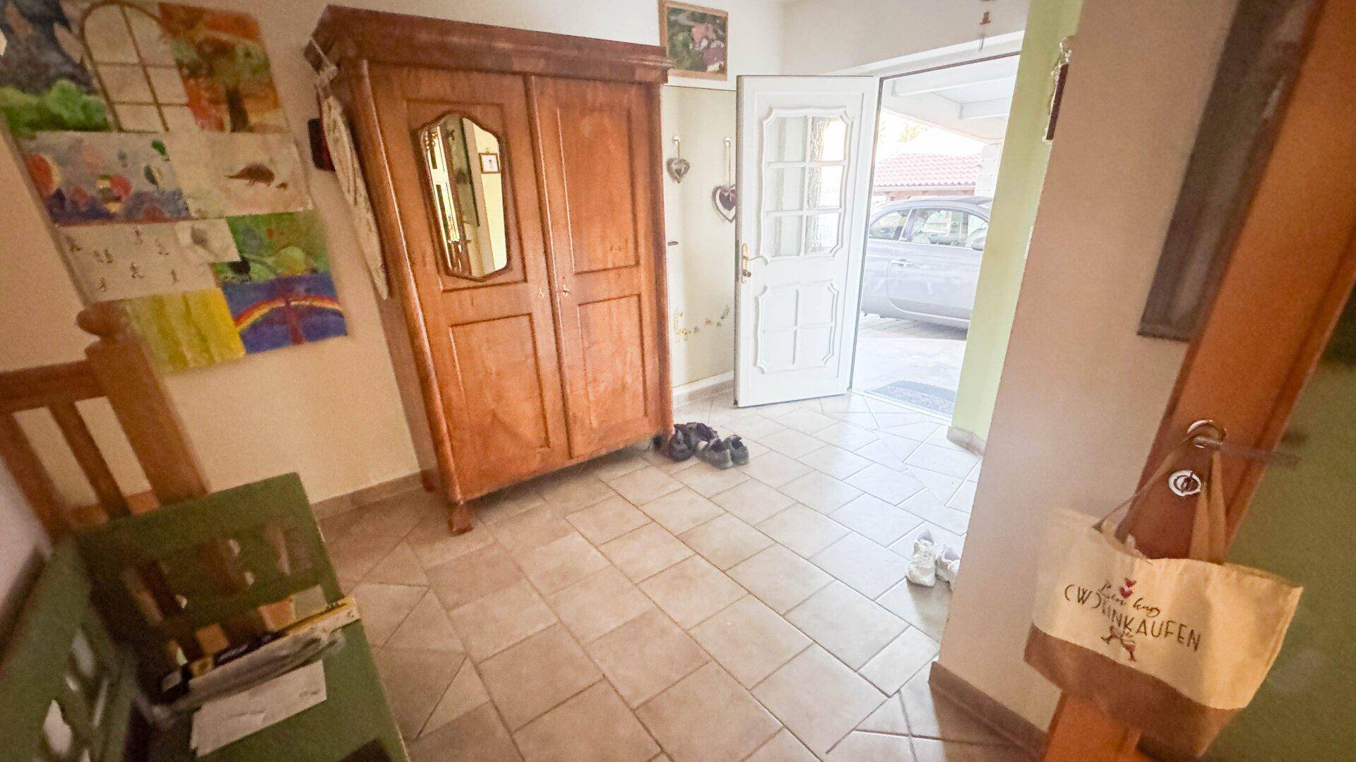 Heller Eingangsbereich mit Fliesenboden, Holzschrank und Blick nach draußen.
