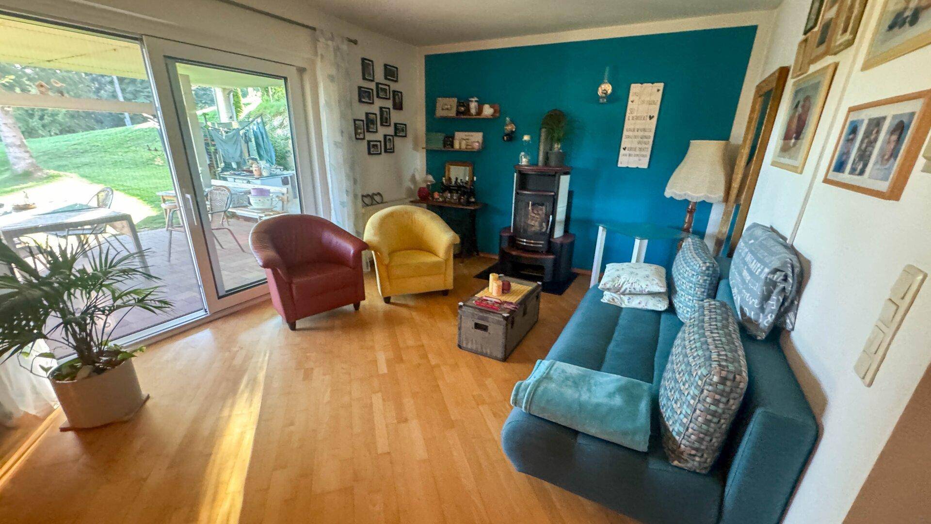Helles Wohnzimmer mit Holzboden, farbiger Wand und Zugang zur Terrasse.