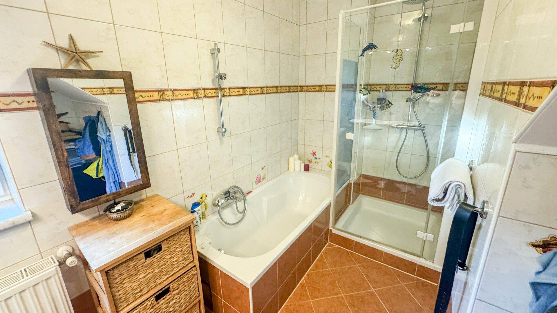 Badezimmer mit Badewanne, Duschkabine und Fliesen in warmen Erdtönen.