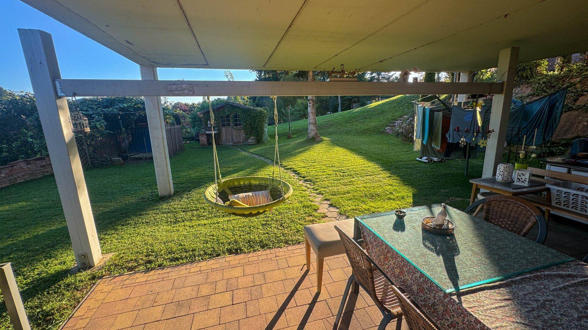 Überdachte Terrasse mit Sitzgelegenheiten, Schaukel und Blick auf den Garten.