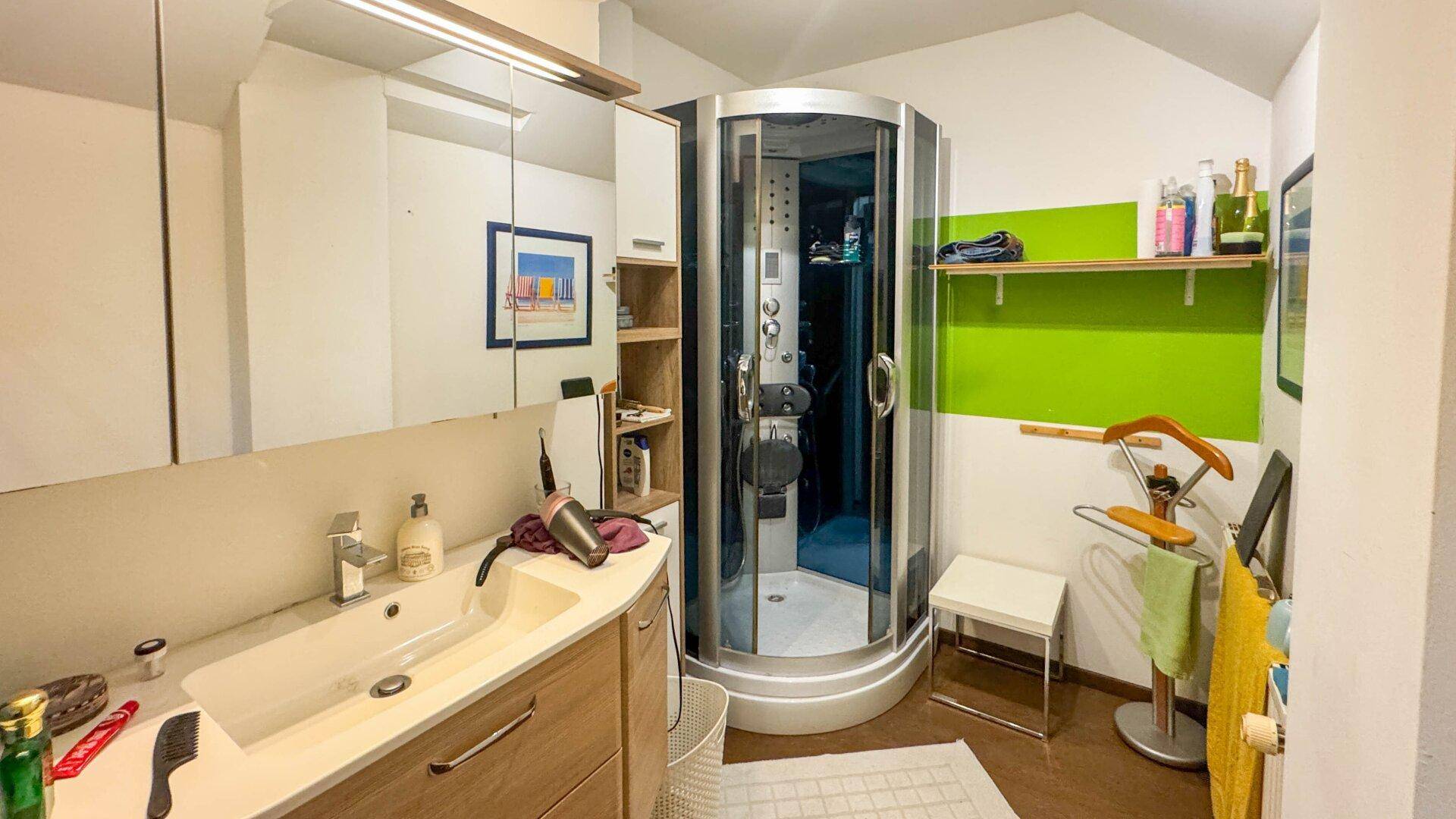 Modernes Badezimmer mit Duschkabine, Waschtisch und grüner Akzentwand.