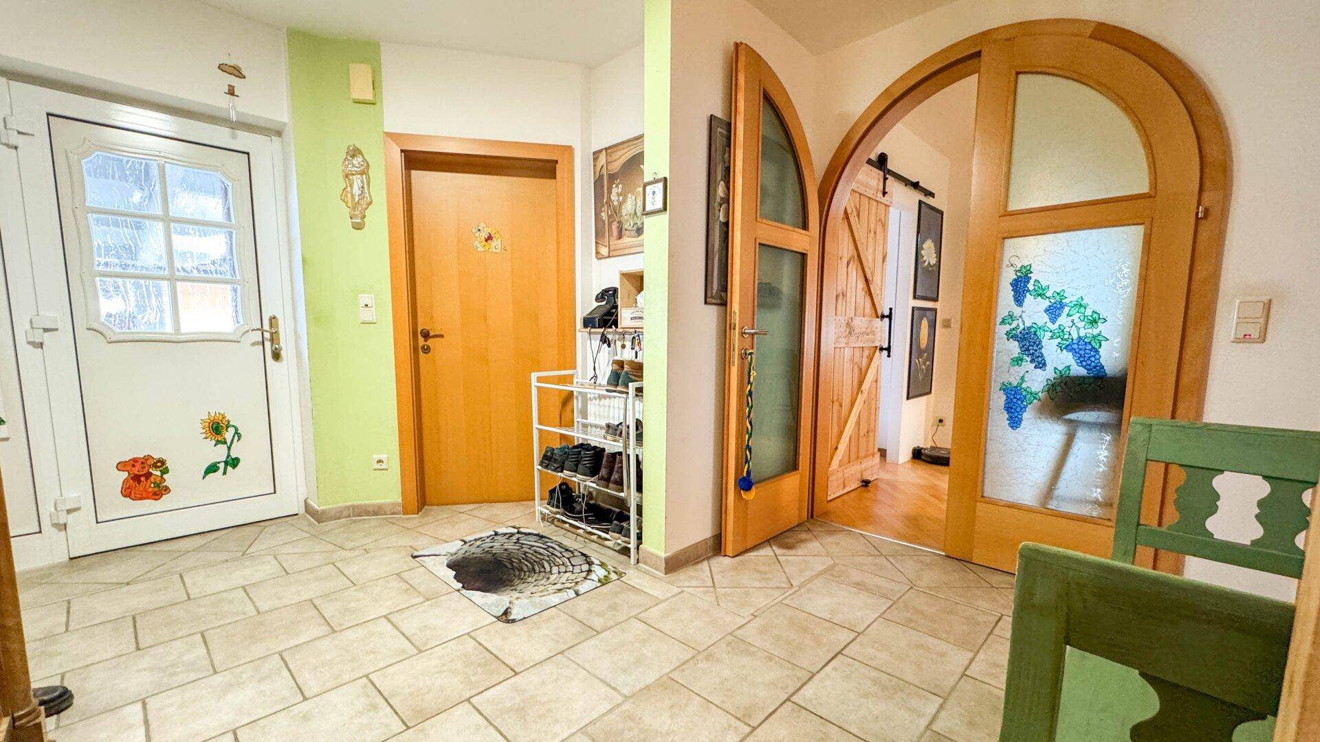 Eingangsbereich mit Fliesenboden, Holztüren und Schuhregal.