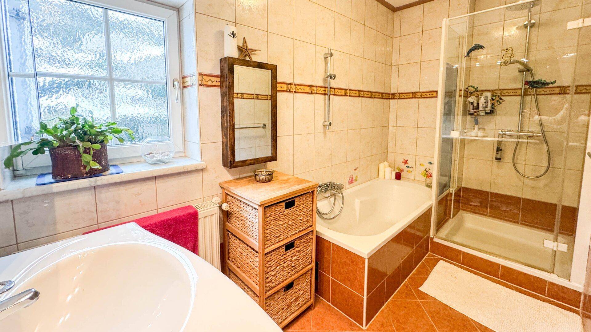Badezimmer mit Badewanne, Duschkabine, Fliesen und Fenster für Tageslicht.