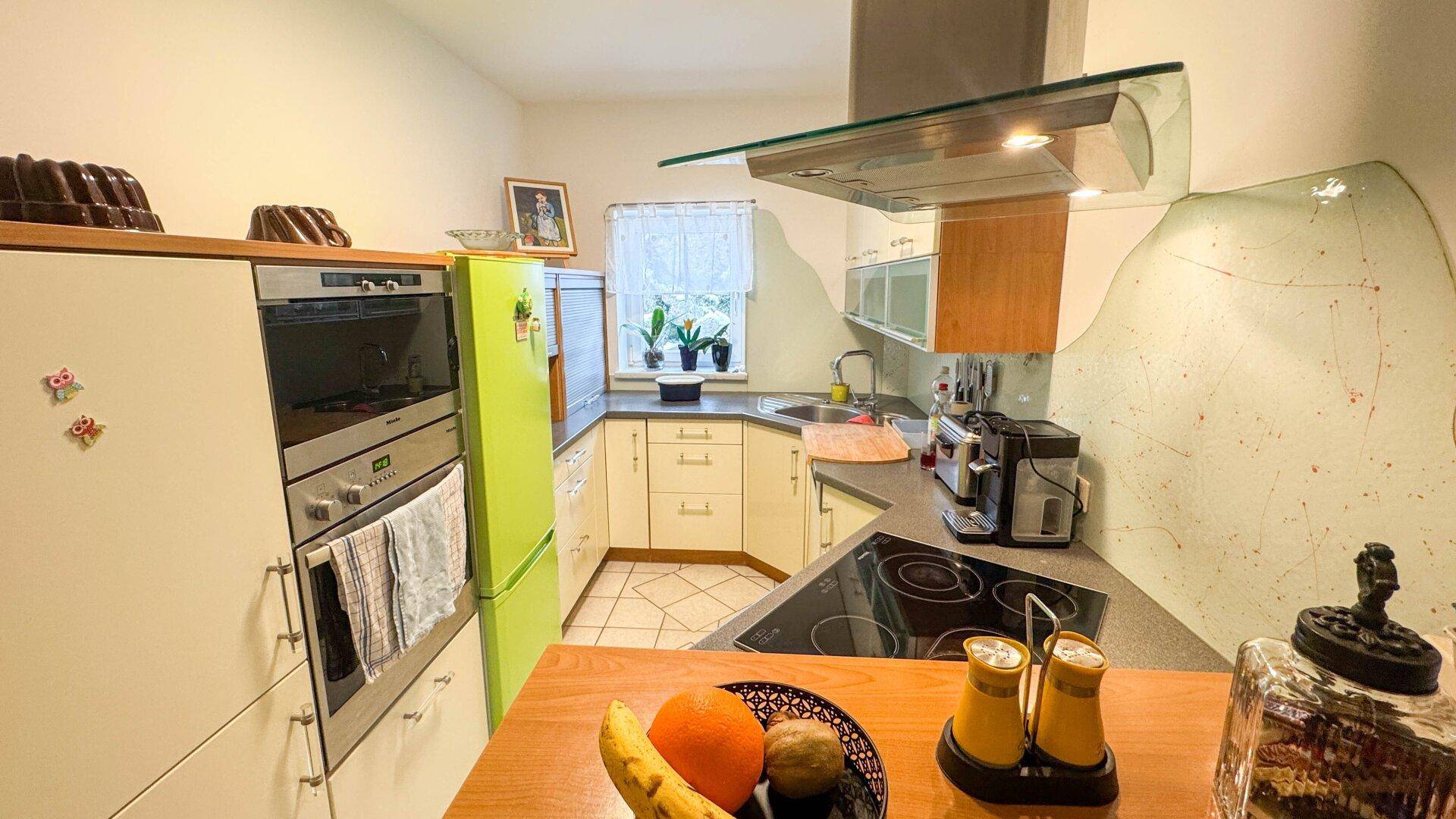 Helle Küche mit Einbaugeräten, grünem Kühlschrank und Kochfeld mit Dunstabzugshaube.