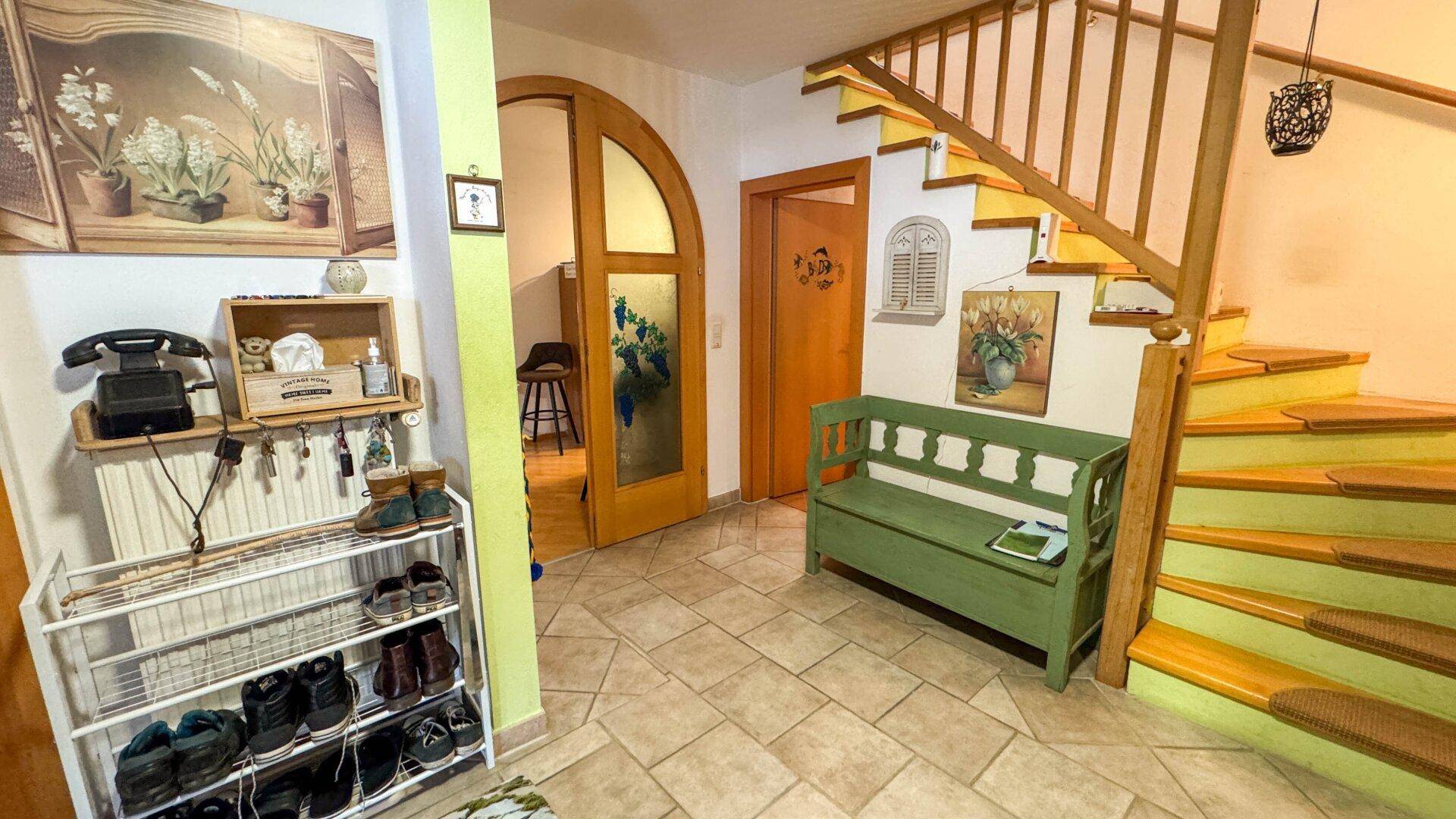 Gemütlicher Eingangsbereich mit Holztreppe, Fliesenboden und einer grünen Sitzbank.