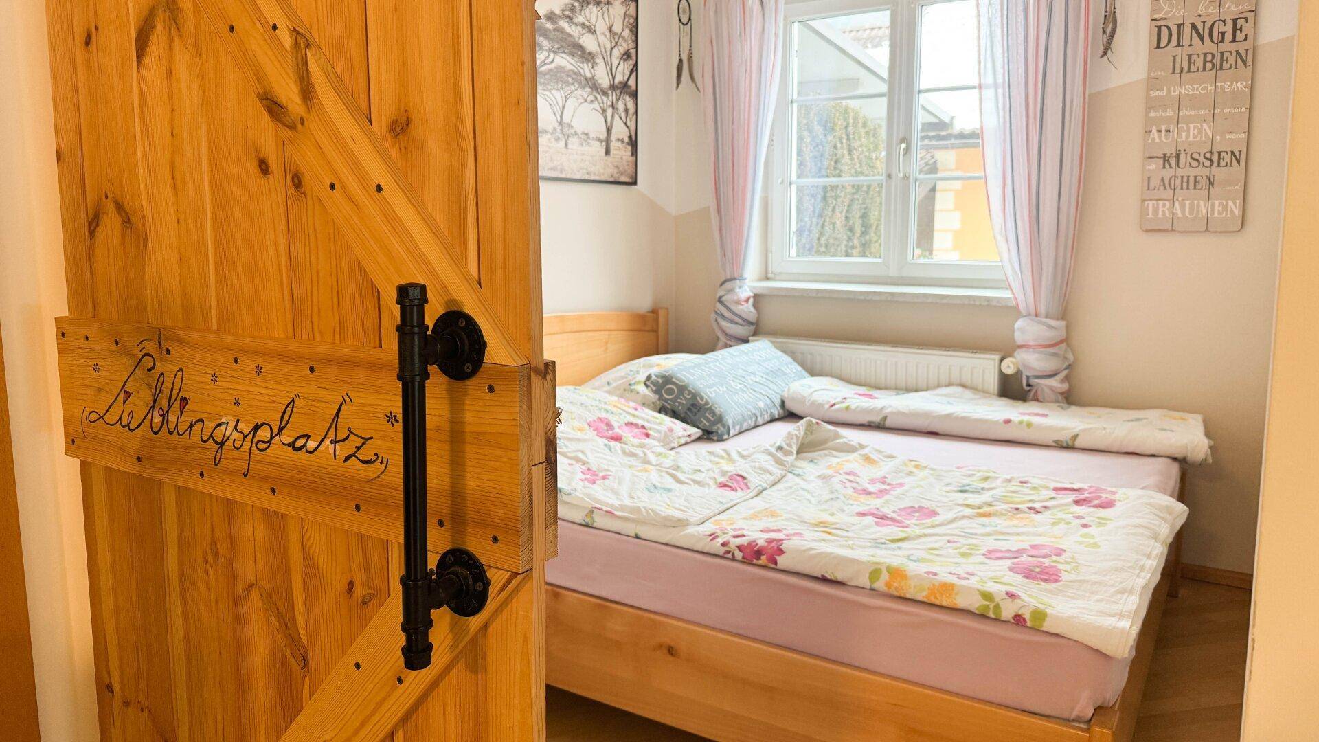 Schlafzimmer mit Holzbett, floraler Bettwäsche und einem Fenster mit Vorhängen.