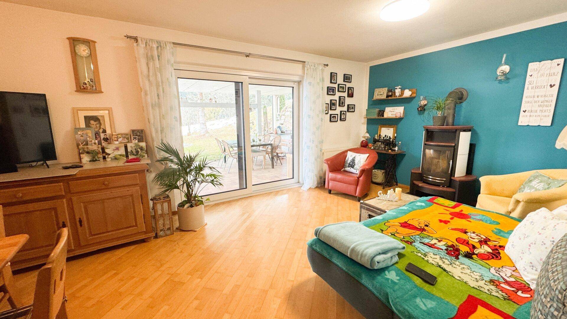 Wohnzimmer mit Holzboden, Kaminofen und Zugang zu einer Terrasse oder Garten.