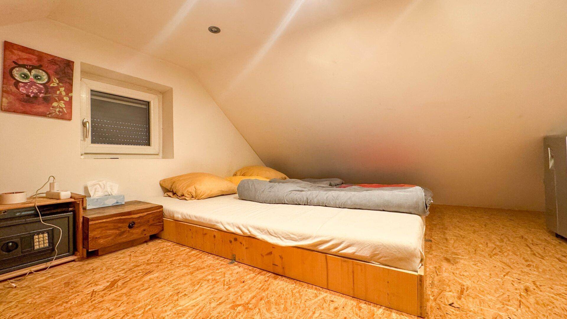 Gemütliches Schlafzimmer im Dachgeschoss mit niedrigem Bett und kleinem Fenster.