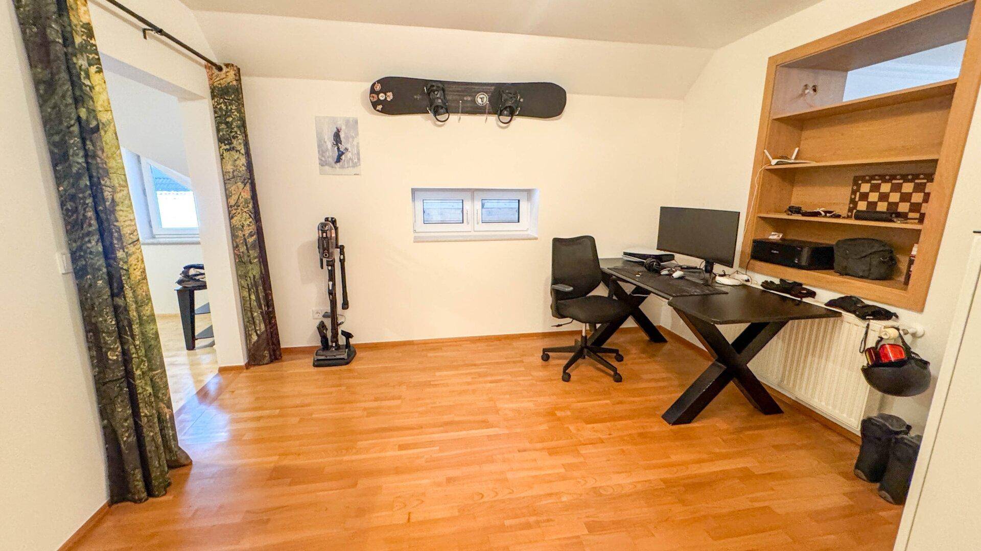 Arbeitszimmer mit Holzboden, Schreibtisch und einem Fenster mit Blick ins Grüne.