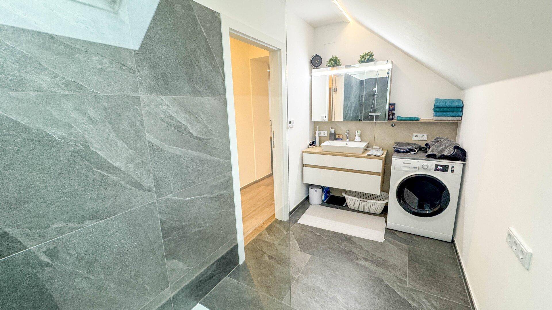 Modernes Badezimmer mit großformatigen Fliesen, Waschmaschine und Dachschräge.
